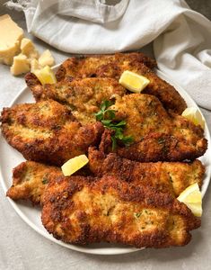 some fried food on a white plate with lemon wedges and parmesan cheese