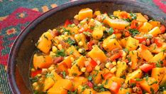 a bowl filled with lots of food on top of a colorful table cloth next to a wooden spoon