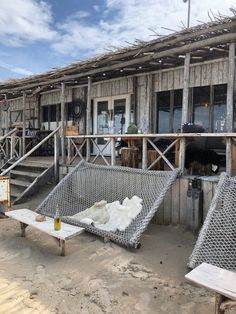 an old wooden building with two chairs and a table in front of it on the beach