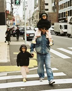 a man walking across a cross walk with a child on his shoulders