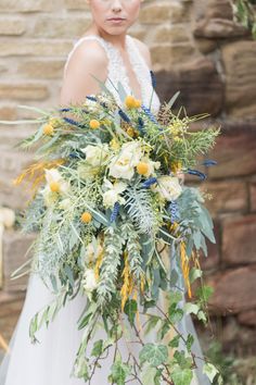 a woman in a wedding dress holding a large bouquet with yellow flowers and greenery