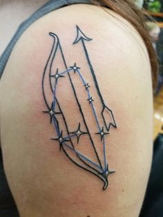 an arrow tattoo on the back of a woman's shoulder, with stars around it