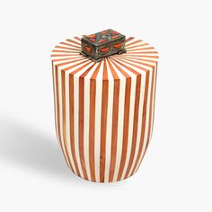 an orange and white striped vase with a small box on top of it's lid