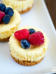 three small desserts on a white plate with raspberries and blueberries in the middle