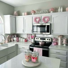 a kitchen filled with lots of white cabinets and pink decorations on the counter top next to an oven