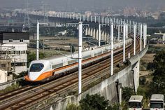 an orange and white train traveling down tracks next to tall buildings with power lines in the background