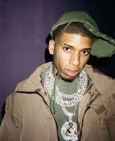 a young man wearing a green hat and jacket with multiple necklaces on his neck