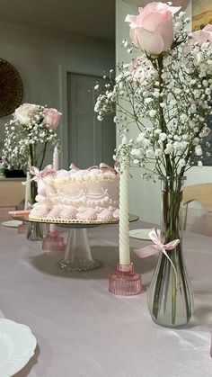 two vases filled with flowers on top of a table next to a white cake