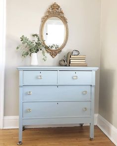 a blue dresser sitting in front of a mirror and plant on top of the dresser