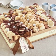 a box filled with lots of cookies next to two cups and saucers on a table