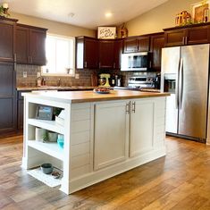 a large kitchen with wooden floors and white cabinetry on the island, along with stainless steel appliances