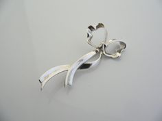 Overview:Offered for sale is a wonderful and very pretty Tiffany and Co. Sterling Silver Ribbon Brooch / Pin. The piece is made from bright and substantial Tiffany silver fashioned to look like a flowing bow / ribbon - very striking and pretty! In excellent condition, this piece is one that you will turn to very often to jazz up your wardrobe. It is no longer produced, and thus makes a great addition for any Tiffany collector. The piece has a perfectly working locking mechanism, and is fully hal Ribbon Brooch, Silver Ribbon, Bow Brooch, Bow Ribbon, Gift Love, Tiffany And Co, Ribbon Bow, Ribbon Bows, Tiffany & Co.