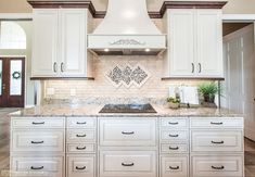 a kitchen with white cabinets and marble counter tops