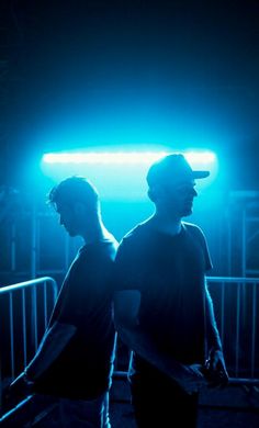 two men standing next to each other in front of a blue and green light at night