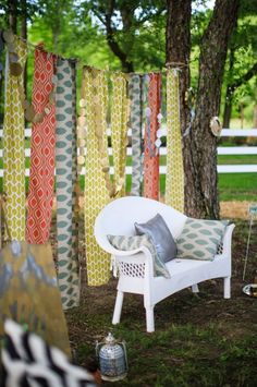 a white chair sitting next to a tree covered in colorful fabric hanging from it's sides