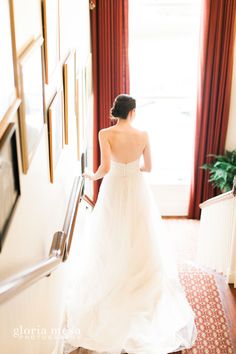 a woman in a white dress is walking down the stairs with her hand on the railing