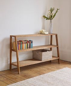 a wooden shelf with books on it next to a white rug and a vase filled with flowers