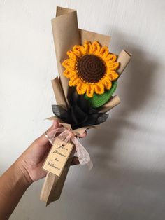 a hand holding a brown paper bag with a sunflower on it and a tag attached to it