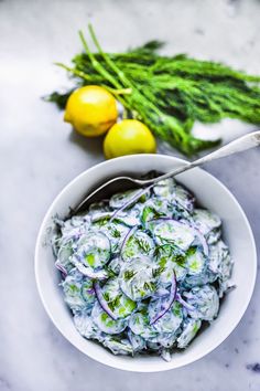 a white bowl filled with salad next to lemons and celery on a table