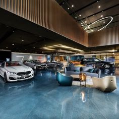 several cars are parked in a showroom next to couches and tables with lamps on them