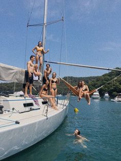 a group of people hanging out on a sailboat in the water with one man swimming