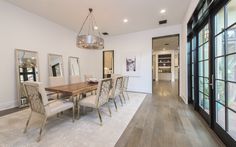 a dining room table with white chairs and large mirrors on the wall next to it