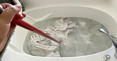 a person is using a red brush to wash their hands in a white sink with water