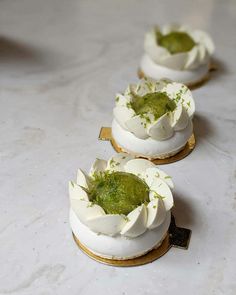 three small cakes with white frosting and green toppings sitting on top of a table