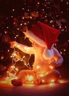 a baby wearing a santa hat sitting in front of a christmas tree with lights on it