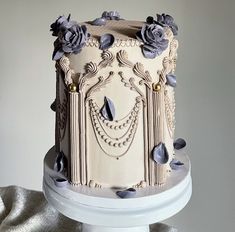 a white cake with blue flowers on it sitting on top of a table next to a silver cloth