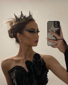 a woman in a black dress is taking a selfie with her cell phone while wearing a tiara