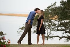 a man and woman kissing in front of a lake