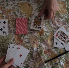 playing cards are being held by two hands on a floral tablecloth with flowers and leaves