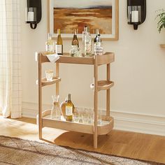 a bar cart with bottles and glasses on it in front of a wall mounted painting