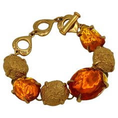 YVES SAINT LAURENT by ROBERT GOOSSENS vintage bracelet featuring gold tone textured oval nuggets embellished with irregular shaped orange resin cabochons. Embossed YVES SAINT LAURENT Made in France. Indicative measurements : adjustable length from approx. 17 cm (6.69 inches) to approx. 22 cm (8.66 inches) / max. width approx. 2.2 cm (0.87 inch). Material : Gold tone metal hardware / Resin. NOTES - This is a preloved vintage item, therefore it might have imperfections. - Colors may differ slightl Ysl Vintage Jewelry, Gold Frosting, Perfect Objects, Ysl Jewelry, Ysl Vintage, Orange Resin, Orange Jewelry, Nugget Bracelet, Vintage Bracelet