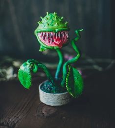 a green plant with an open mouth and sharp teeth on it's head, sitting on a wooden table