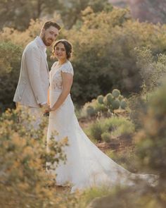 a bride and groom pose for a photo in front of cacti at their wedding