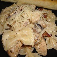 chicken and mushroom pasta on a black plate with a long piece of bread in the background