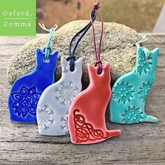 three ceramic cat ornaments are hanging on a string next to a rock with snowflakes