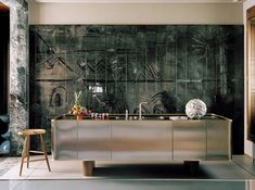 a kitchen with a metallic counter top and stools in front of an artistic wall