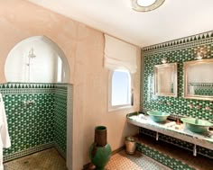 a bathroom with green and white tiles on the walls, two sinks and a mirror