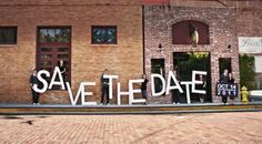 people standing in front of a brick building with the words save the date written on it