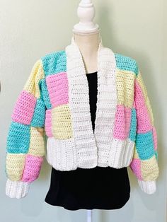 a white mannequin wearing a multicolored knitted jacket on top of a black dress