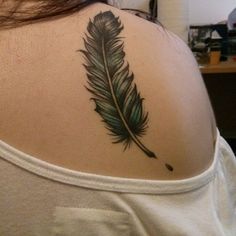 a woman with a tattoo on her back has a green feather in the shape of a heart