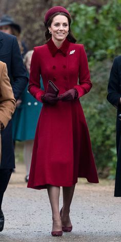 a woman in a red coat and hat walks with other people