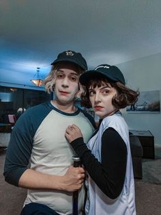 two people dressed up as zombies in a living room with lights on and one person wearing a baseball cap