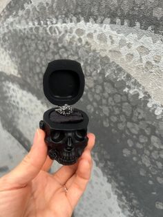 a hand holding a small black skull ring box