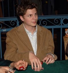 a young man sitting at a table with two other people around him and playing cards