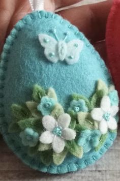 a hand holding a blue felt ornament with flowers on it