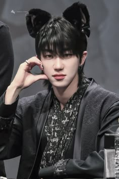 a person sitting at a table with a cat ears on top of their head and one hand near his ear